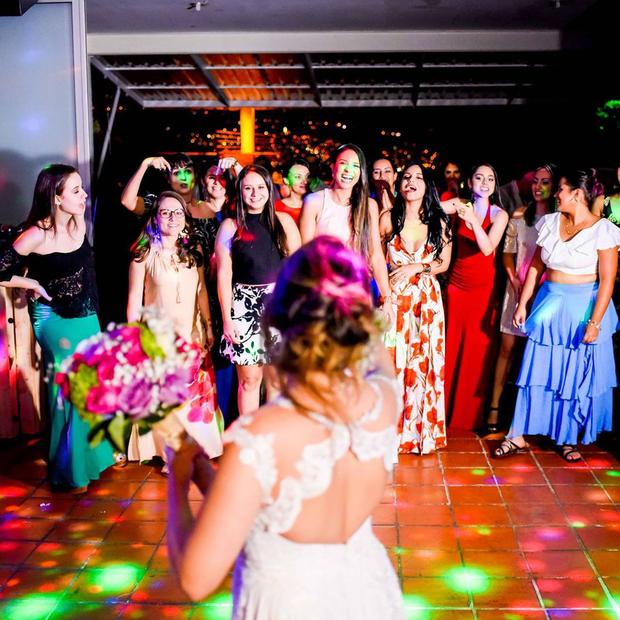 Novia lanzando el ramo a las invitadas en la pista de baile iluminada con luces de colores