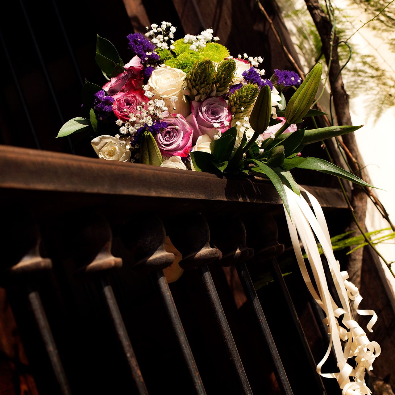 Ramo nupcial con rosas blancas, lilas y fucsia apoyado sobre una baranda de hierro forjado